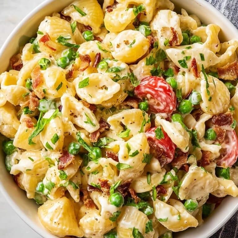 Creamy Pasta Salad with shells, peas, bacon, and cherry tomatoes in a white bowl