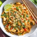 Spicy Chicken Pad Thai garnished with peanuts, lime, and cilantro in a white bowl