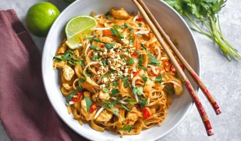 Spicy Chicken Pad Thai garnished with peanuts, lime, and cilantro in a white bowl