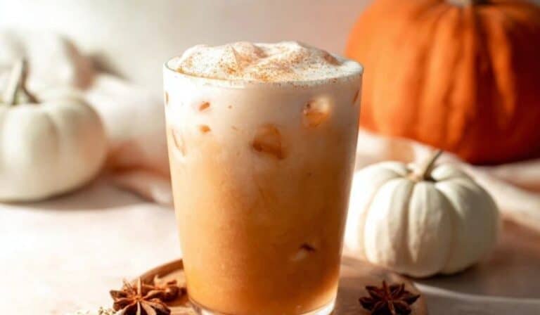 Iced Pumpkin Chai Latte with foam and fall spices on wooden coaster