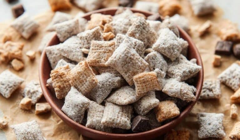 Peanut Butter Puppy Chow in a rustic bowl with powdered sugar and chocolate chunks