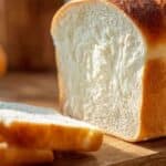 The Best White Bread from Scratch fresh out of the oven with a golden crust on a rustic wooden surface