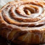 Giant Cinnamon Roll Cake on a wooden table with glaze dripping