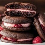 Chocolate Raspberry Sandwich Cookies stacked on a plate with raspberry filling showing