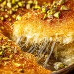 Homemade Lebanese Kanafa in a round pan with a cheesy slice and pistachios on top