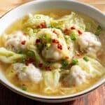 Cabbage and pork dumpling soup in a rustic bowl with scallions and chili oil