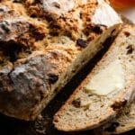 Classic Irish soda bread loaf sliced on a wooden board with butter and marmalade.