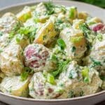 Creamy dill potato salad in a white bowl with fresh dill and red potatoes