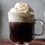 creamy Irish coffee with whiskey in glass mugs topped with whipped cream