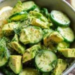 Cucumber avocado lemon salad in a large bowl with fresh herbs on top