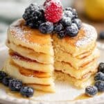 Fluffy lemon ricotta pancakes stacked high with berries and powdered sugar