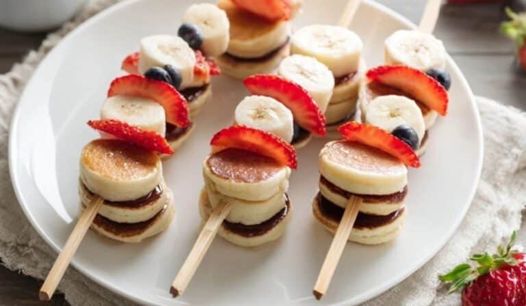 Mini pancake skewers with fruit on a brunch platter with maple syrup