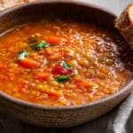 Slow-cooker lentil and tomato soup in a rustic bowl with herbs and bread