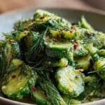 Smashed cucumber and herb salad in a white bowl with fresh herbs