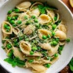 Spring pasta with peas in a white bowl with lemon zest and fresh herbs