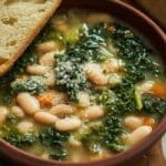 White bean and kale soup in a rustic bowl with bread on a wooden table